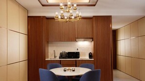 A modern kitchen with wooden paneling, a round dining table with blue chairs, and a chandelier. - Royal M Al Aqah Beach Hotel And Resort by Gewan (Al Aqah)