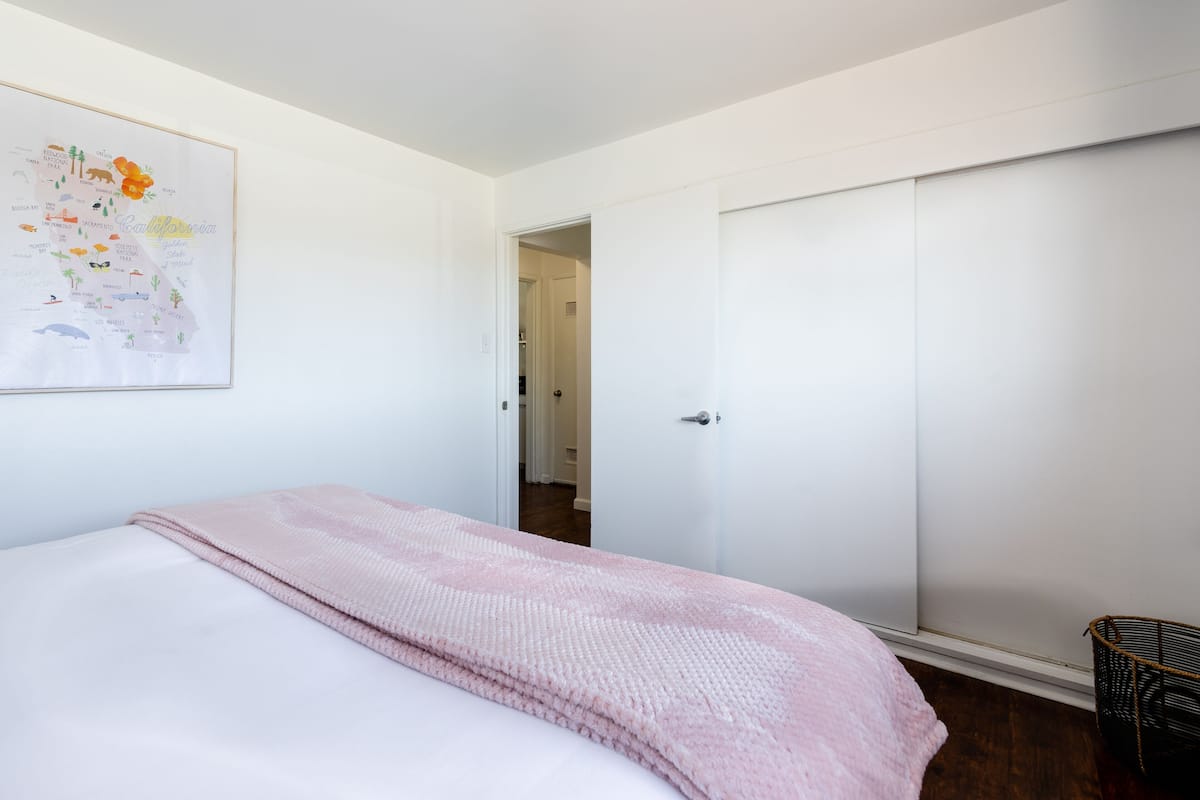 Ein Schlafzimmer mit einem Bett, einer rosa Decke, einer Karte an der Wand und einem Kleiderschrank.