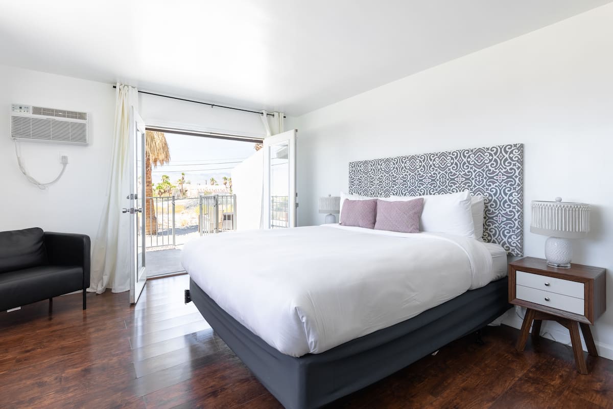 Ein modernes Schlafzimmer mit einem großen Bett, einem Nachttisch, einem schwarzen Sofa und Blick ins Freie.