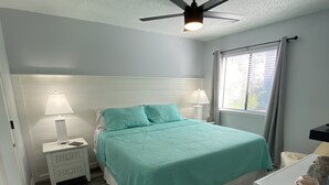 A bedroom with a bed, a nightstand, a lamp, a ceiling fan, a window with curtains, and a small table with a decorative item. - Minutes to beach and golf courses (Myrtle BEach)