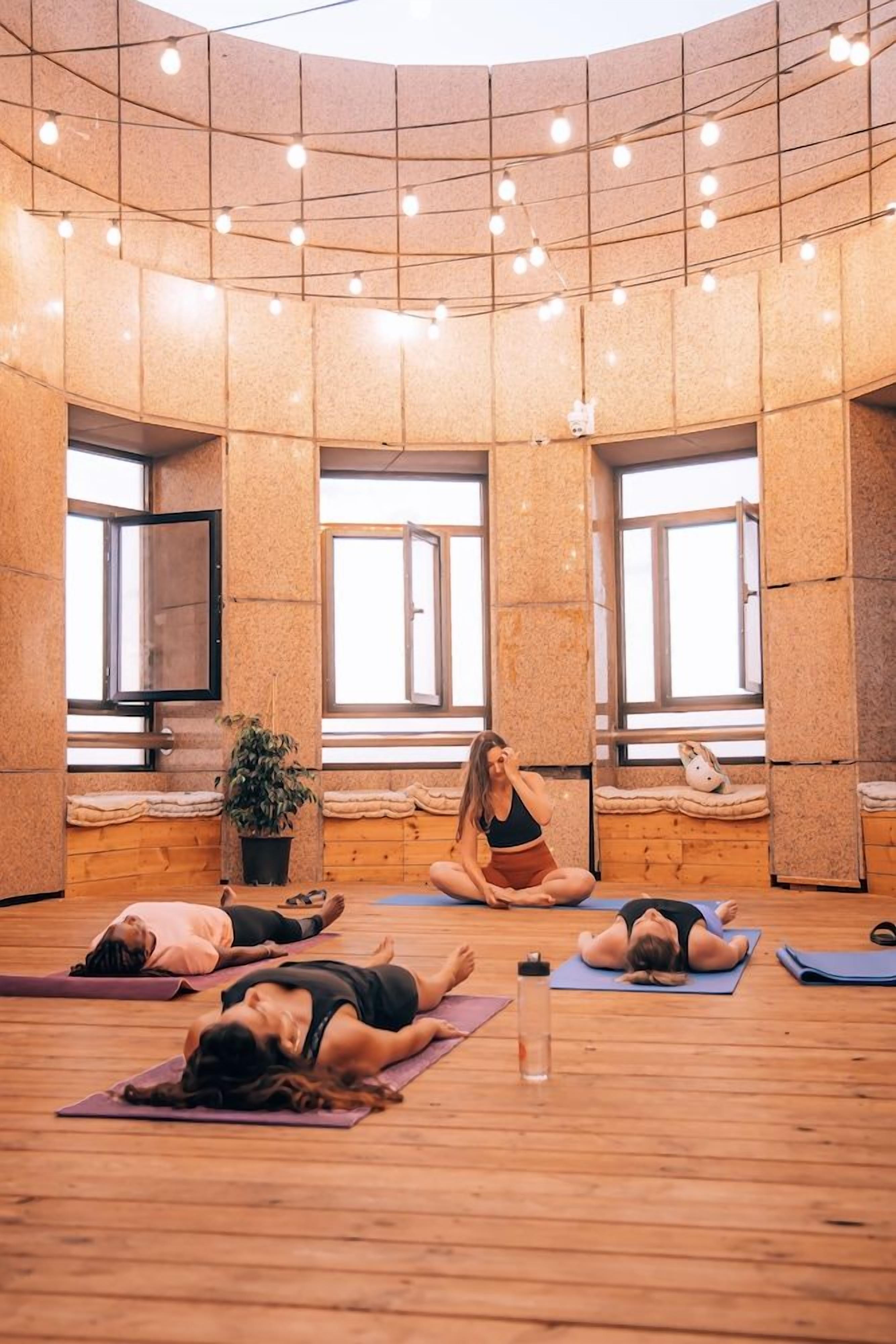 Un estudio de yoga con suelo de madera, ventanas amplias y luces colgantes.