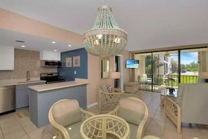 A modern kitchen with a central island, a dining area with wicker furniture, and a large chandelier.