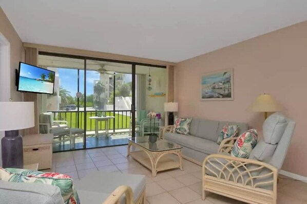 Un salon avec un canapé, une table basse et un téléviseur, un balcon avec vue sur la mer et un tableau accroché au mur.