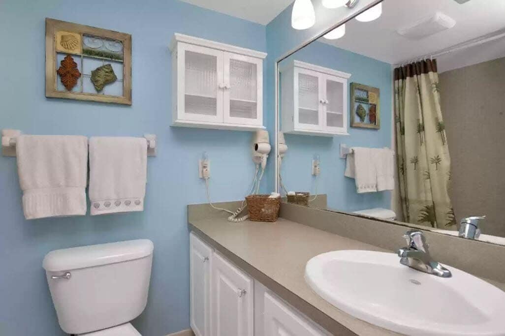 A bathroom with a toilet, a sink, a mirror, and a shower curtain.