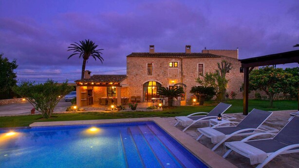 Una villa de piedra con piscina, mobiliario de exterior y un patio bien iluminado.