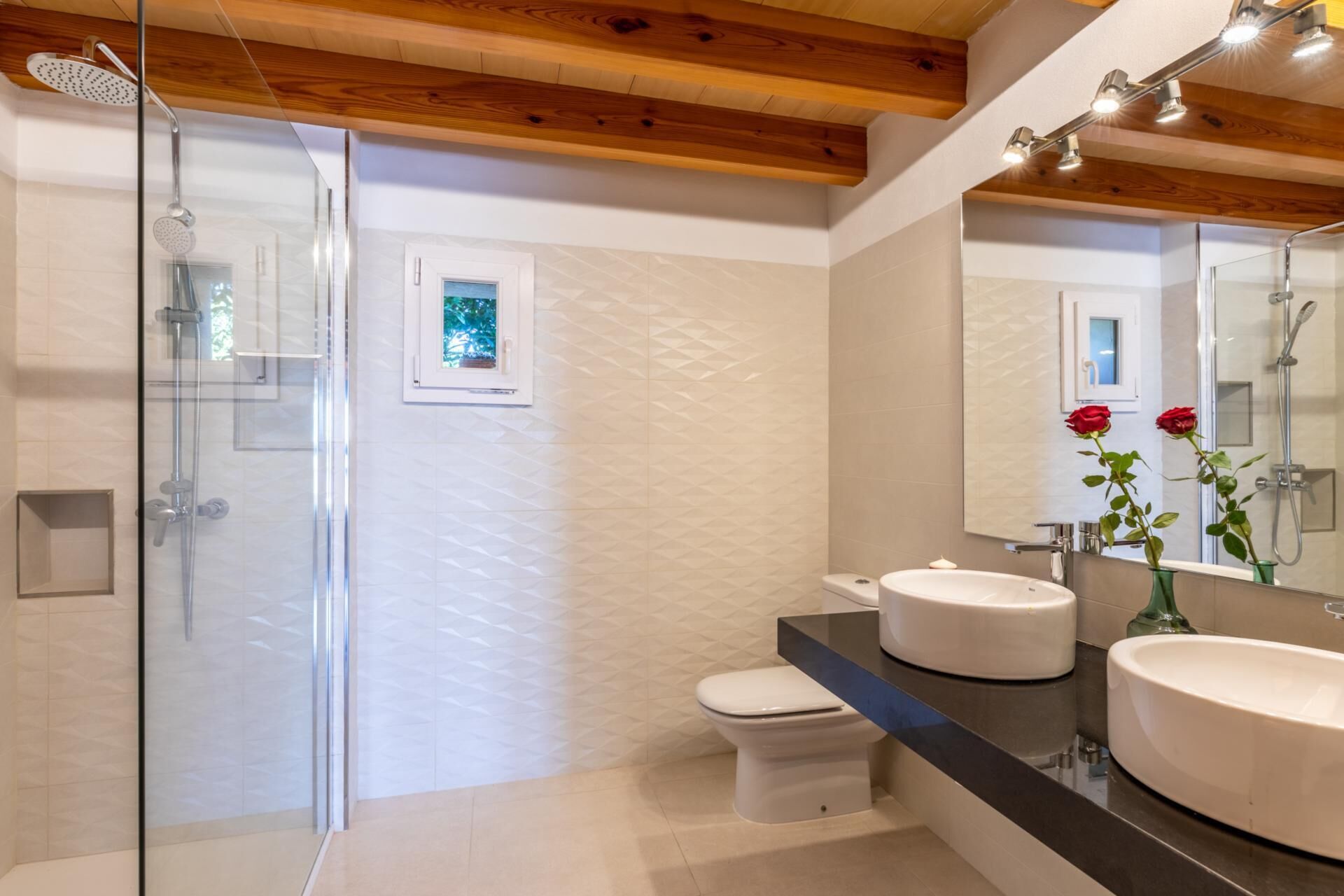 Un baño moderno con cabina de ducha de vidrio, inodoro y dos lavamanos.