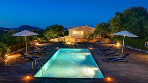 Ein Pool mit Liegestühlen und Sonnenschirmen, umgeben von einer Holzterrasse und einem Steinhaus.