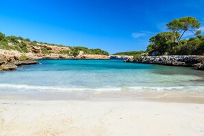 Una playa con agua turquesa cristalina, orilla arenosa y acantilados rocosos con vegetación.