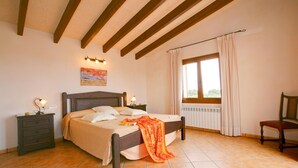 Una camera da letto con un letto, comodini, una sedia, una finestra con tende e un termosifone.