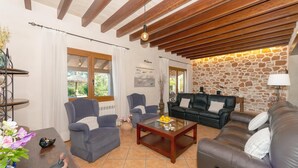 Un soggiorno con parete in pietra, travi in legno a soffitto, un divano in pelle nera, due poltrone grigie e un tavolino da caffè.