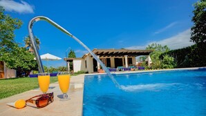 En swimmingpool med en fontän, två glas apelsinjuice och ett par solglasögon på poolområdet.