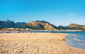 Ein Strand mit Liegestühlen und Sonnenschirmen, einem klaren Himmel und Bergen im Hintergrund.