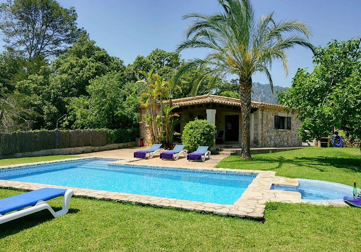 A swimming pool with lounge chairs, a stone building, and surrounding greenery.