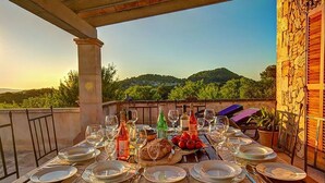 Ein Tisch ist für eine Mahlzeit gedeckt, mit Weinflaschen, Tellern und einem Tomatenkorb, mit Blick auf eine reizvolle Landschaft.
