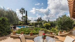 A poolside area with a glass table and chairs, surrounded by potted plants and a clear view of a swimming pool. - Adorable Family Villa, A/C, Beautiful Landscaped Garden, Private Pool close to Pollença & Beaches! (Pollença)