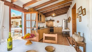 A rustic kitchen with wooden beams, a dining area with a table set for two, and a view of the outside patio. - Adorable Family Villa, A/C, Beautiful Landscaped Garden, Private Pool close to Pollença & Beaches! (Pollença)