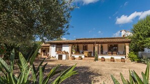 A traditional Mediterranean-style house with a tiled roof, a patio with outdoor seating, and a garden with large-leafed plants. - Adorable Family Villa, A/C, Beautiful Landscaped Garden, Private Pool close to Pollença & Beaches! (Pollença)