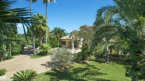 A house surrounded by lush greenery, including palm trees and flowering plants. - Fantastic Spacious Villa, A/C, Big Private Pool, Idyllic Location - 5/10 mins to Towns & Beaches! (Alcudia)