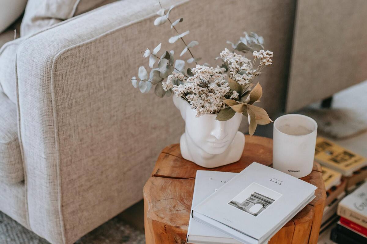 A cozy living room with a beige sofa, a wooden coffee table with a vase of flowers and a candle, and a few books.