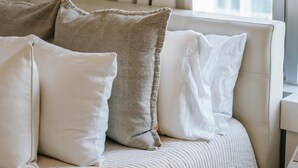 A bed with a beige quilt and pillows, a bedside lamp, and a window with curtains. - The Boardwalk Beach House (Santa Cruz)