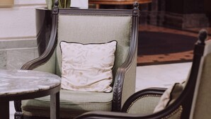 A green upholstered chair with a decorative pillow, a round table, and a potted plant in a lobby area. - The Boardwalk Beach House (Santa Cruz)