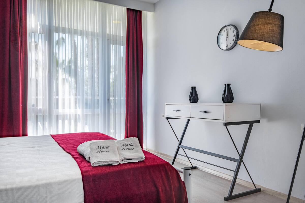A hotel room with a bed, a desk, a lamp, and a clock on the wall.