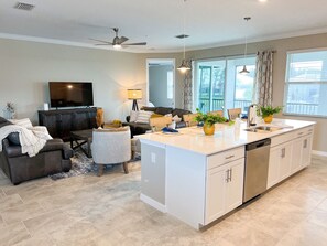 Een moderne keuken met een centraal eiland, een zithoek met een bank, en een woonkamer met een televisie.