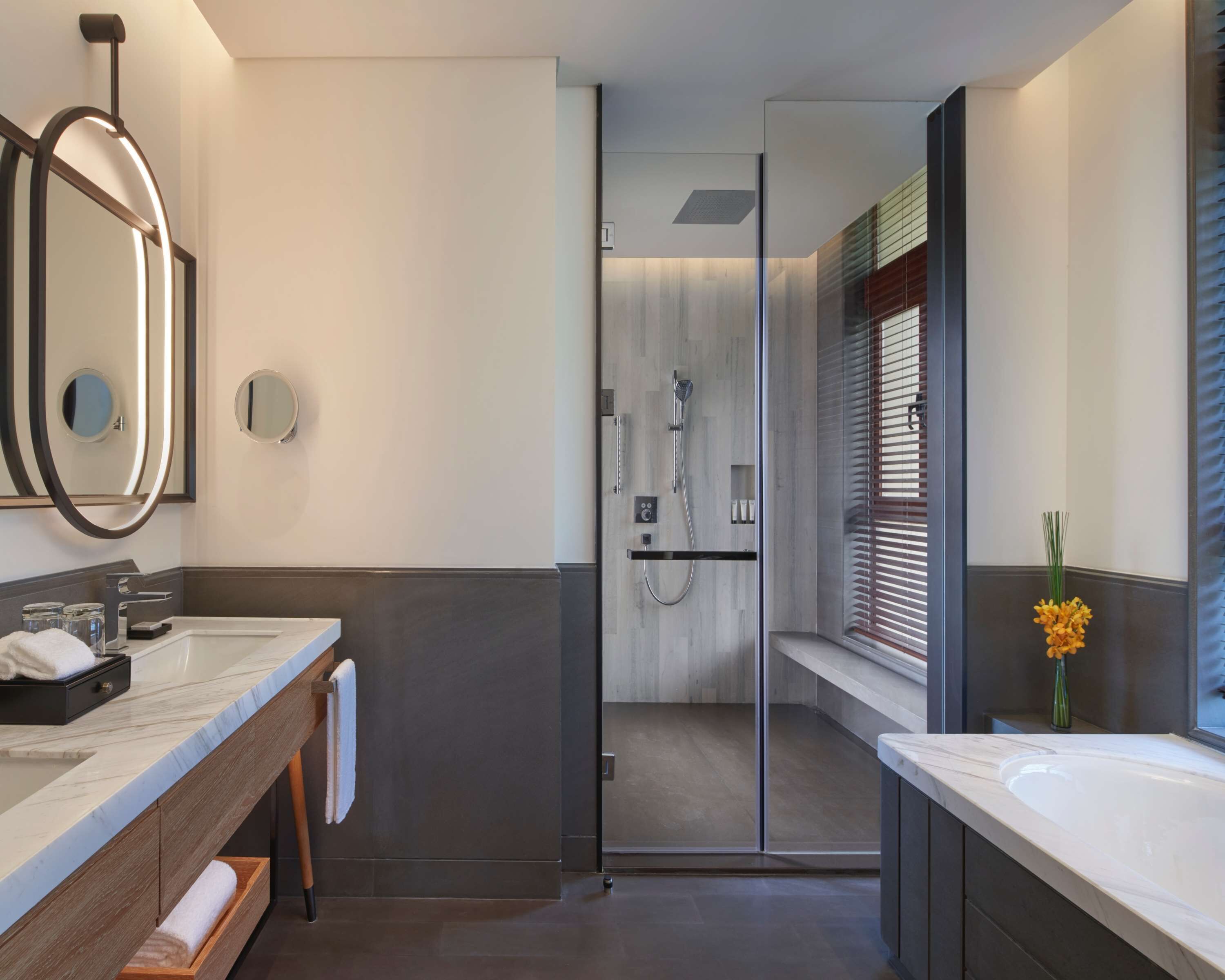 Une salle de bain moderne avec deux vasques, une douche à l’italienne en verre et un grand miroir.
