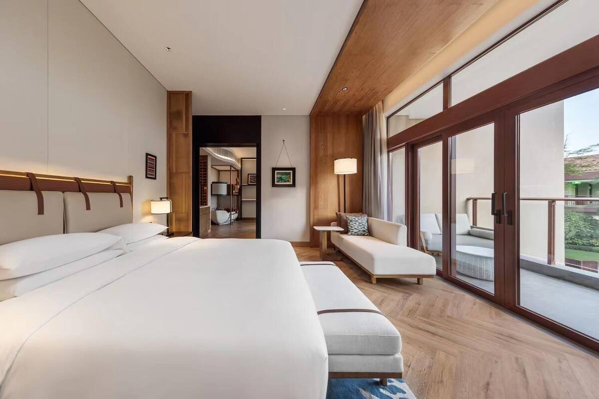 Moderni hotellihuone, jossa on suuri sänky, sohva ja parveke, jolta on näkymä.