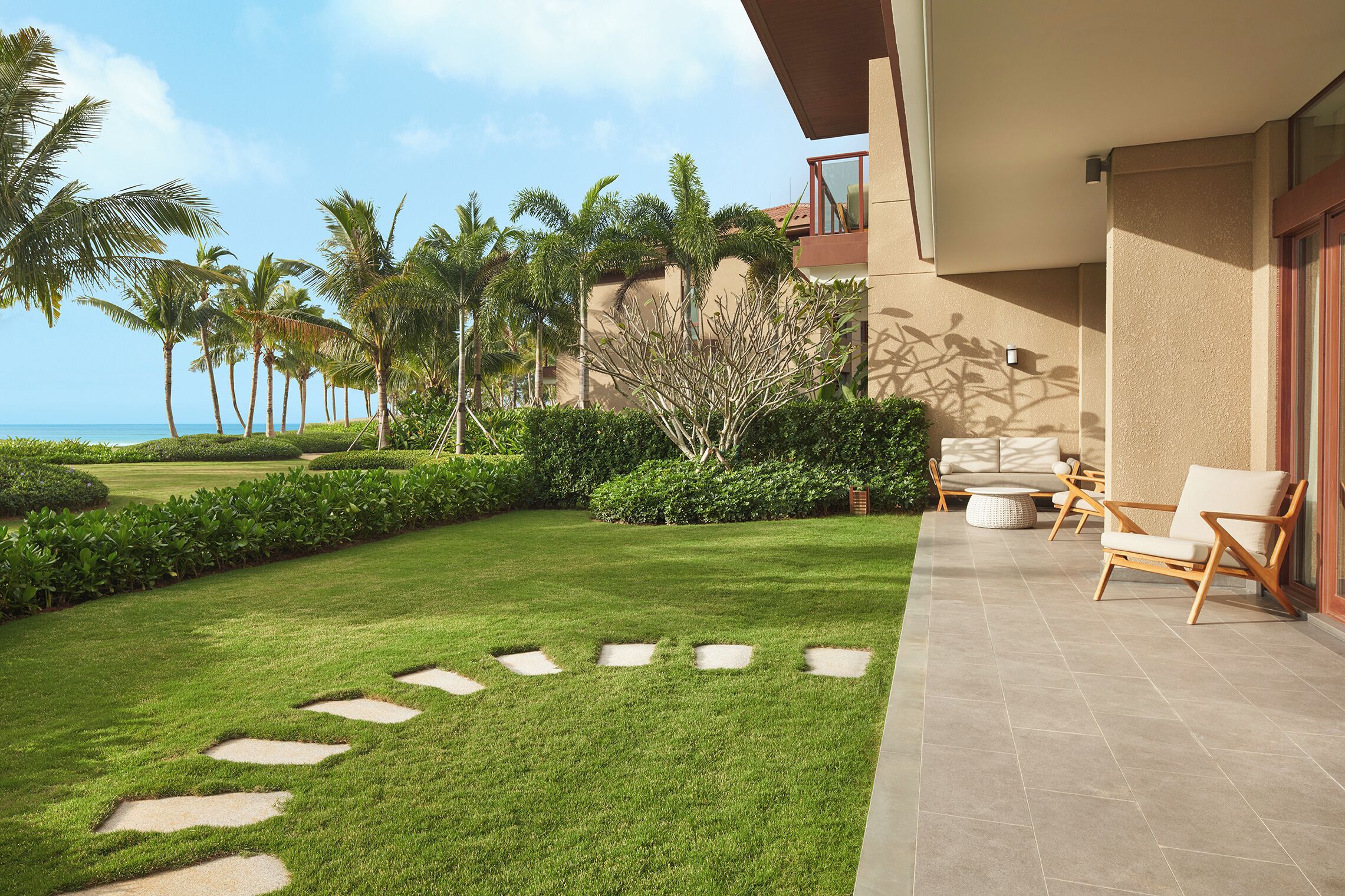 A well-maintained lawn with stepping stones, a patio with outdoor furniture, and a view of the ocean.