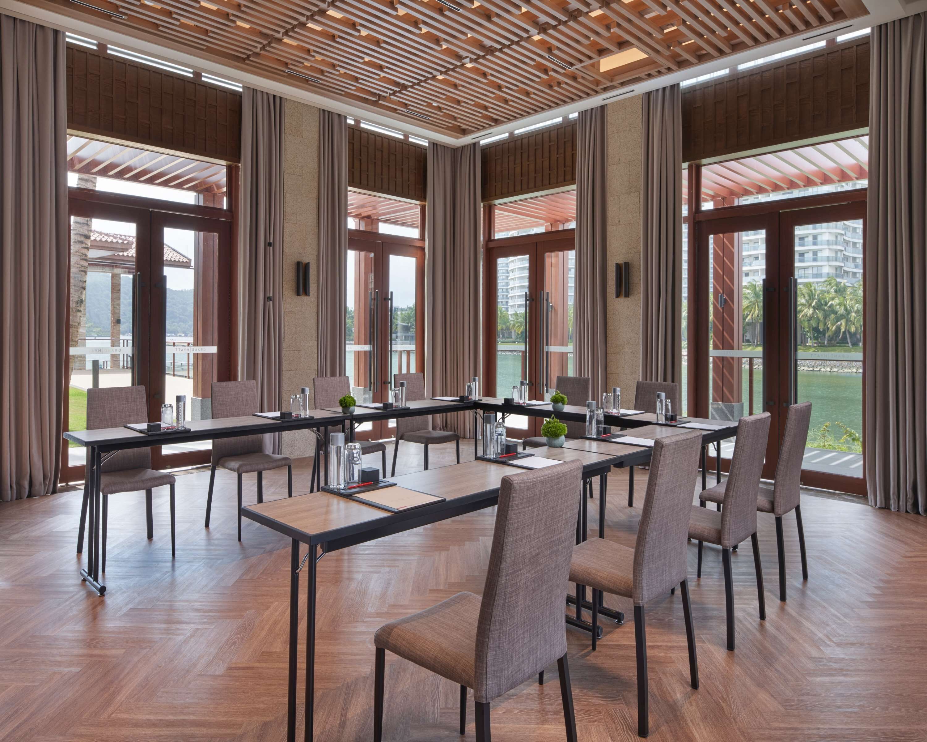A conference room with a long table, chairs, and large windows offering a view of the outdoors.