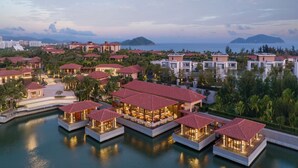 Un complex turístic amb nombroses bungalous sobre l'aigua, comunicats per passos, una marina i una vista del mar i muntanyes allunyades.