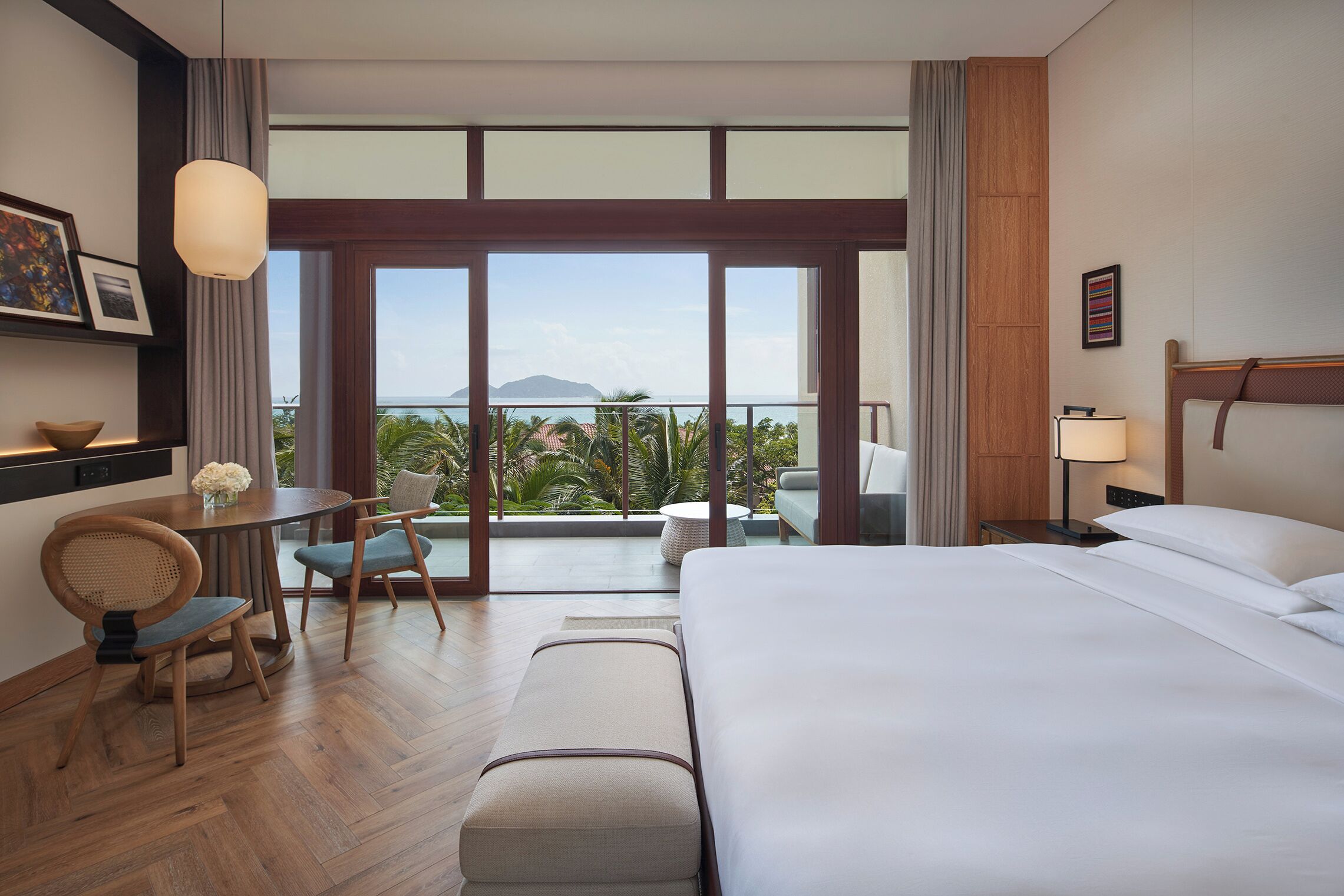 Une chambre d’hôtel comprenant un lit, un bureau avec une chaise, une petite table avec un vase et une vue sur l’extérieur.