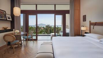 Une chambre d’hôtel comprenant un lit, un bureau avec une chaise, une petite table avec un vase et une vue sur l’extérieur.