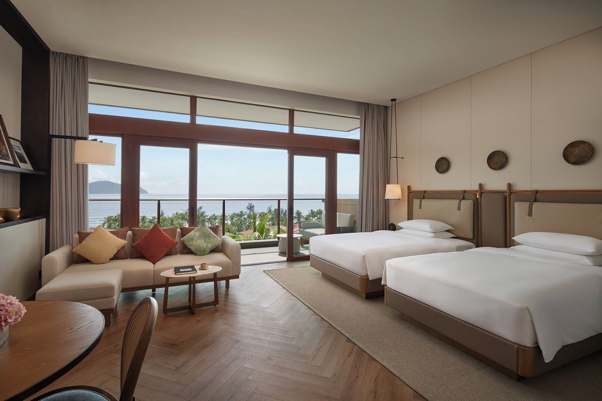 Une chambre d’hôtel avec un balcon, un canapé, deux lits et un coin repas.