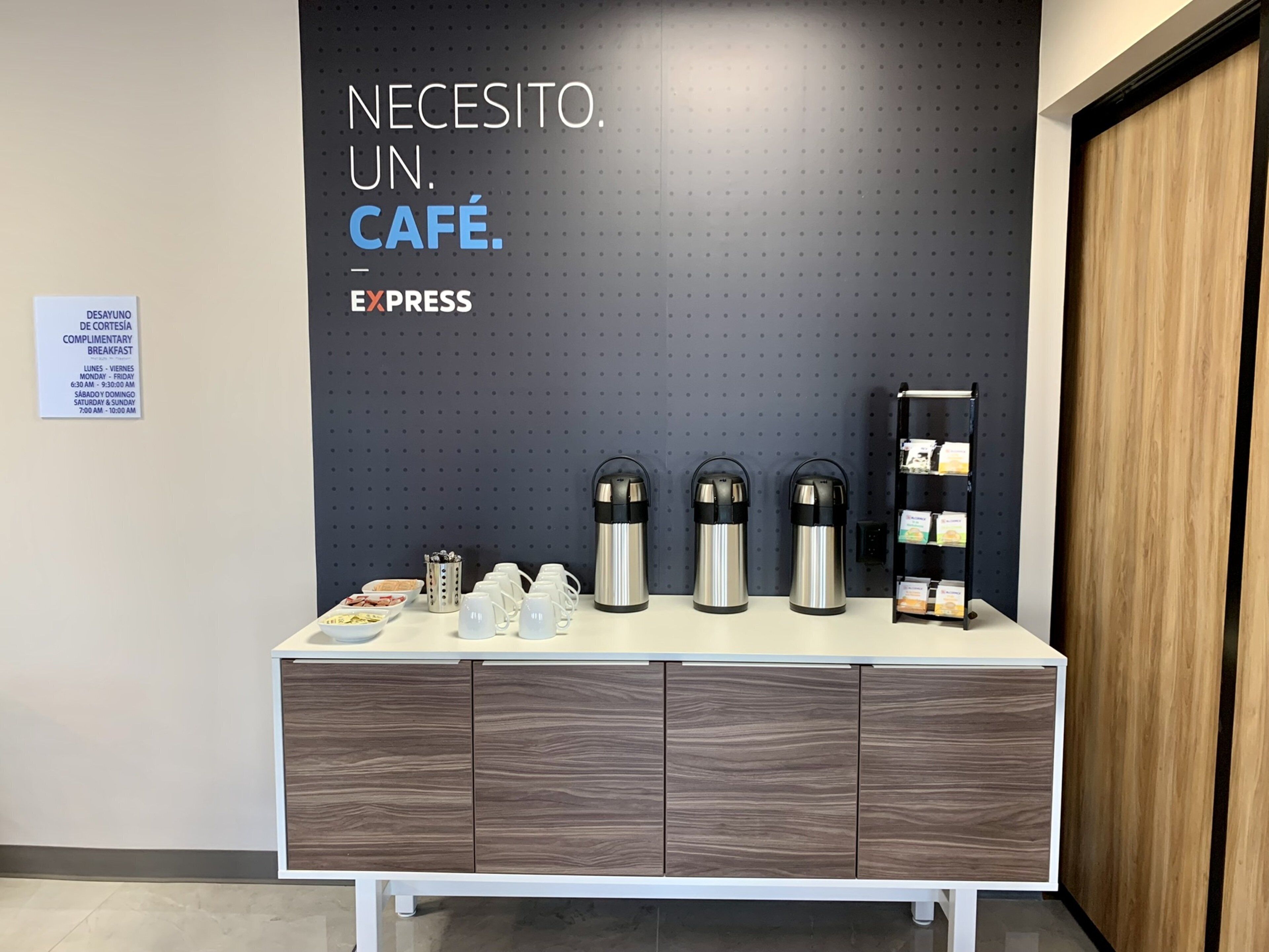 A café setup with a sign reading "NECESITO. UN. CAFÉ. EXPRESS" and a complimentary breakfast sign.