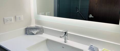 Un baño moderno con un lavabo blanco, un espejo y una ducha que se ve en el fondo.