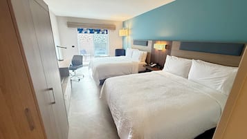 Una habitación de hotel con dos camas, un escritorio, una silla y una ventana con vistas.