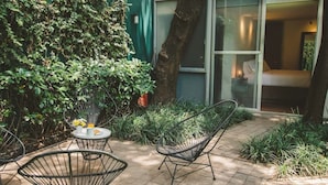 Une terrasse extérieure avec une table et des chaises, entourée de verdure et bordée d’un bâtiment doté d’une porte-fenêtre coulissante.