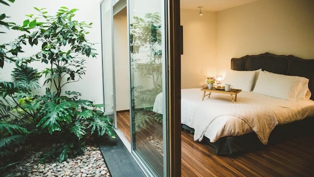 Une chambre à coucher avec un lit, une table de chevet et une vue sur un jardin, visible à travers une porte vitrée.