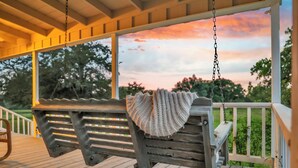 A wooden porch with a swing and a bench, overlooking a garden and a sunset. - Luxury Round Top Farmhouse  / 6mil to The Square (Round Top)