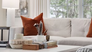 A living room with a sofa, a coffee table with books and decorative items, a lamp, and a window with a view of trees. - Luxury Round Top Farmhouse  / 6mil to The Square (Round Top)