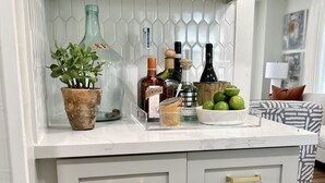 A kitchen with white cabinets, gold handles, and a countertop with various items including a potted plant, bottles, and a bowl of fruit. - Luxury Round Top Farmhouse  / 6mil to The Square (Round Top)