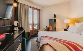 Et hotelværelse med seng, skrivebord, stol, lampe, natbord og udsigt over det fri.