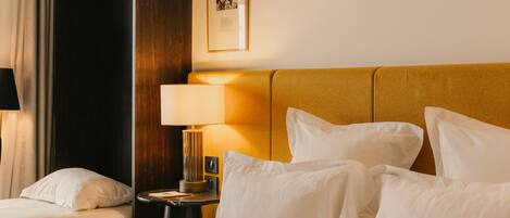 Une chambre d’hôtel avec un lit, des oreillers, une table de chevet avec une lampe, un tableau encadré au mur et une porte sombre.