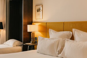 Ein Hotelzimmer mit Bett, Kissen, einem Nachttisch mit Lampe, einem gerahmten Bild an der Wand und einer dunklen Tür.