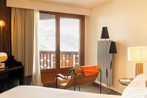 Habitación de hotel con cama, una silla, escritorio, lámpara y ventana con vista a un paisaje nevado.