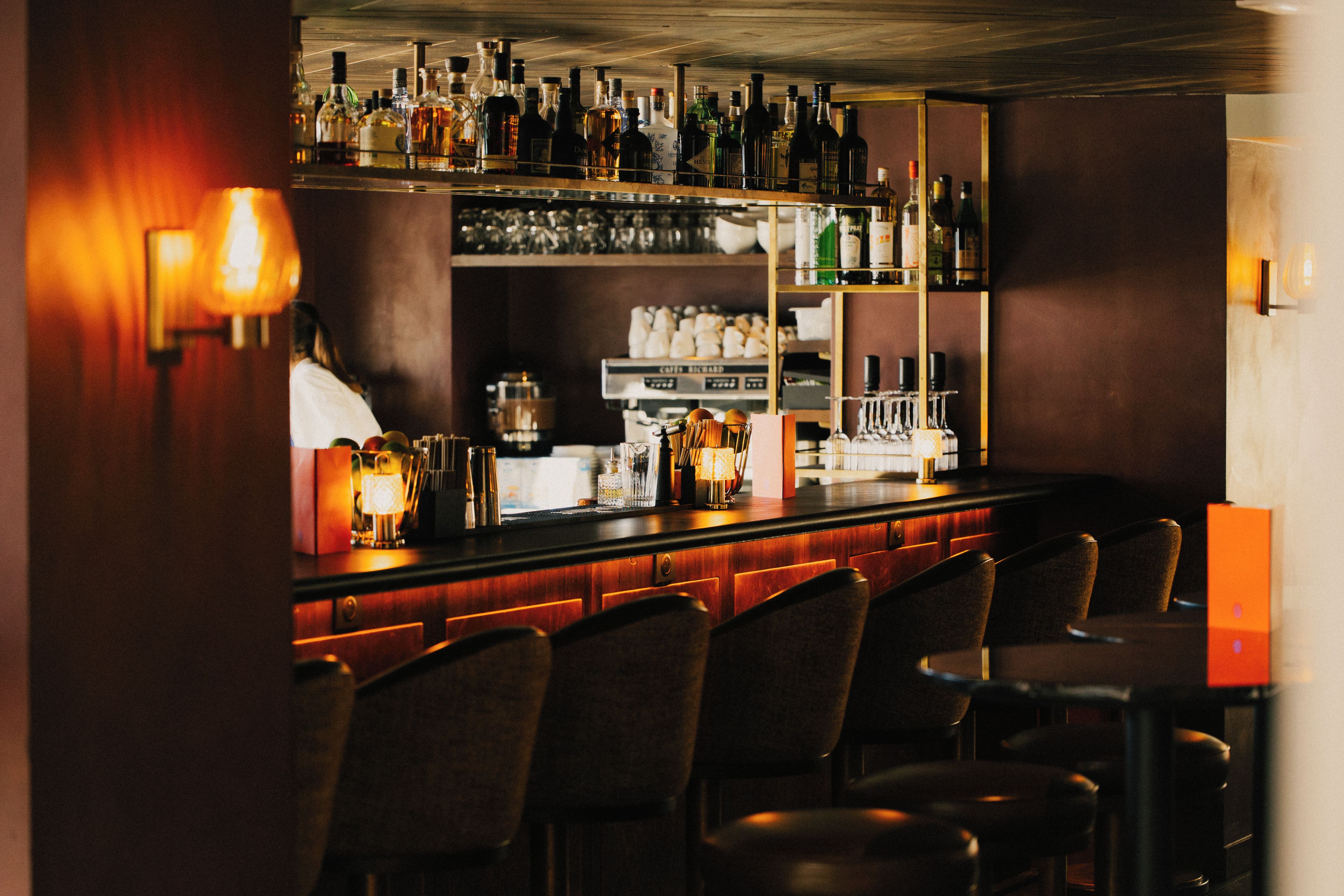 A bar area with multiple shelves of bottles, a bar counter, and several chairs.