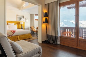 Una habitació d'hotel amb un llit, un sofà, un escriptori, una làmpada, una finestra amb cortines i vista a una muntanya nevada.