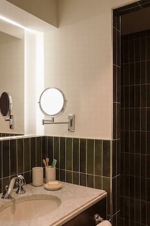 Un baño con un lavabo, dos espejos, un perchero para toallas y una taza con cepillos de dientes.
